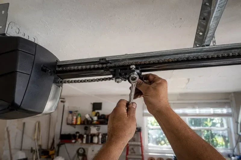 Hands holding a wrench against an opener trolley beneath a chain rail — Chain-Drive Opener Repair, Georgina