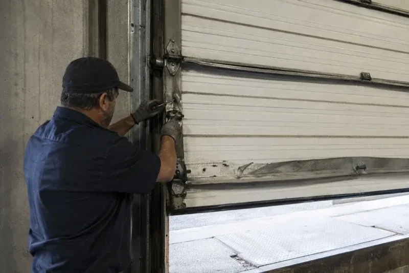 Person holding tools at the side hinge of a partly raised industrial sectional door — Commercial Sectional Door Repair, Georgina