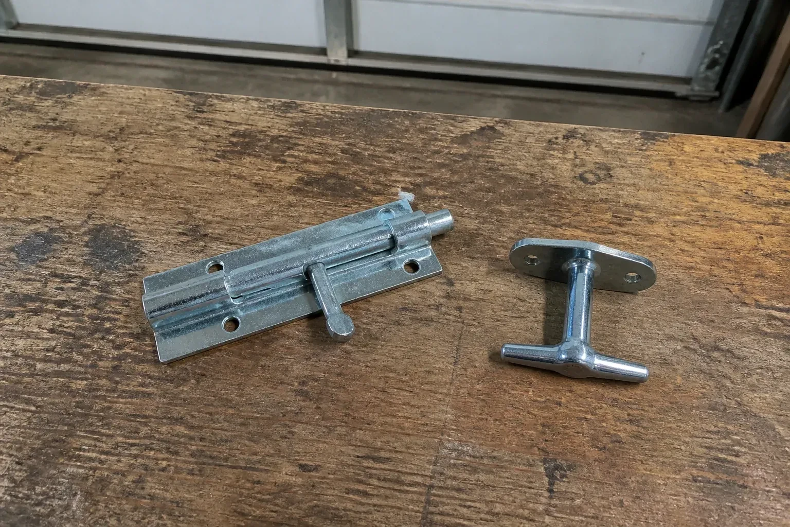 Detached slide bolt and T-handle on a wooden garage workbench. — Garage Door Manual Lock Repair, Georgina