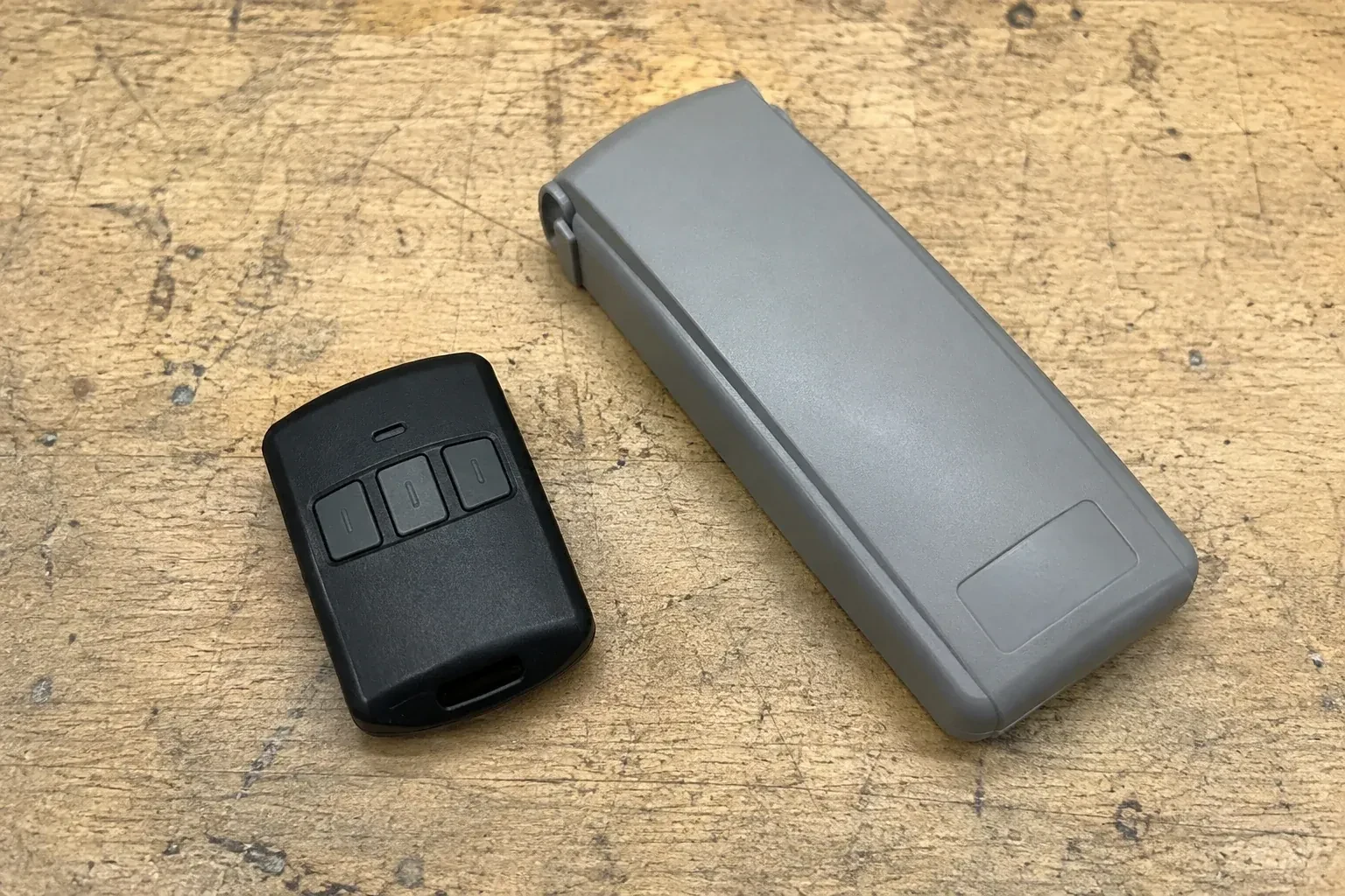 Three-button remote beside a closed grey keypad cover on a workbench. — Garage Door Remote and Keypad Programming, Georgina