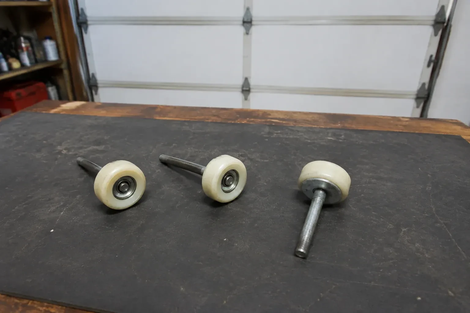 Three detached nylon-wheel garage door rollers with steel stems on a work mat. — Garage Door Roller Replacement, Georgina